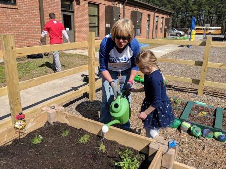 An educator helps a child water plants in a school garden