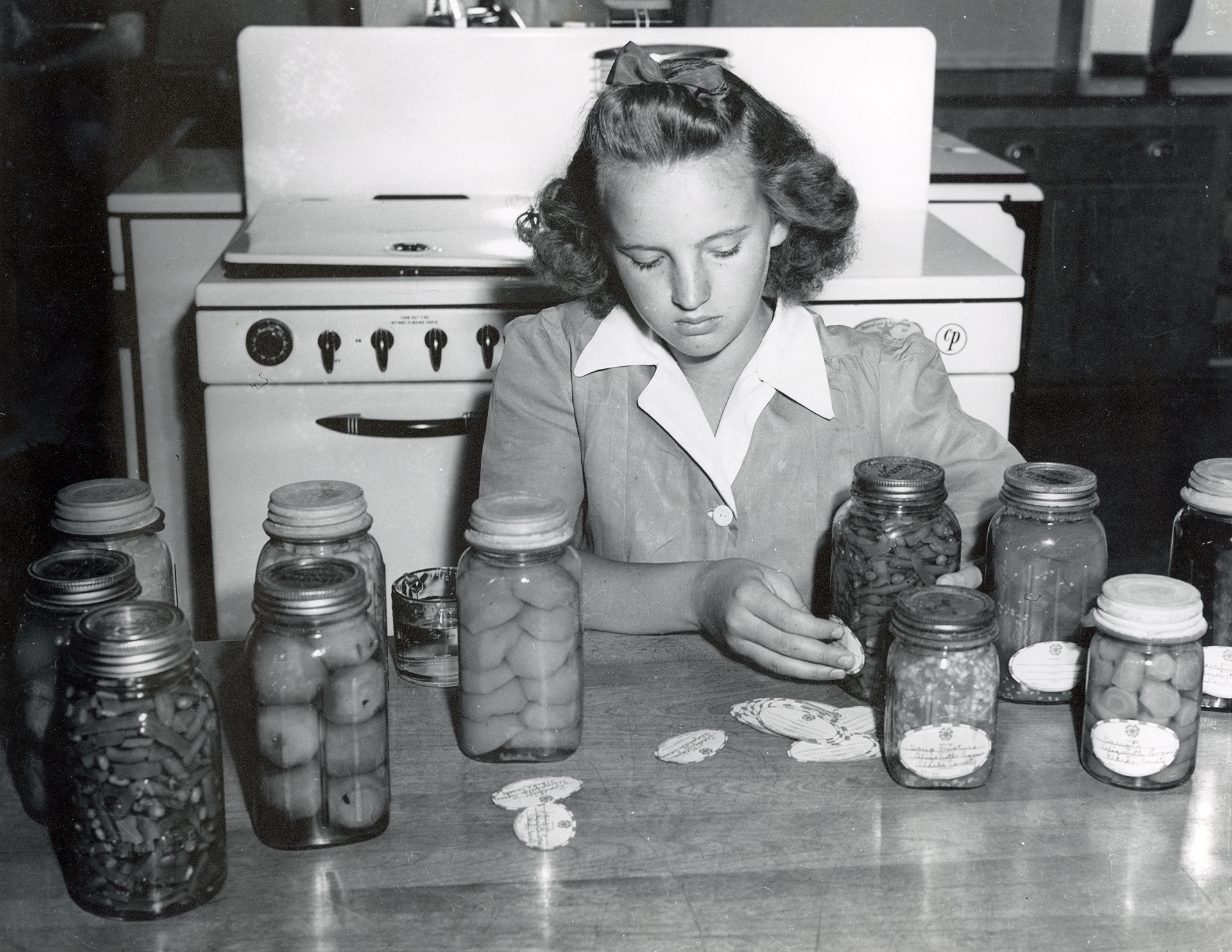 A girl puts labels on jars of preserved fruits and vegetables